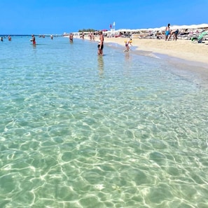 Een strand met helder, ondiep water, mensen die zwemmen en strandparasols.