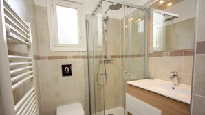 Un baño moderno con ducha envuelta en vidrio, inodoro blanco y tocador de madera con lavamanos.
