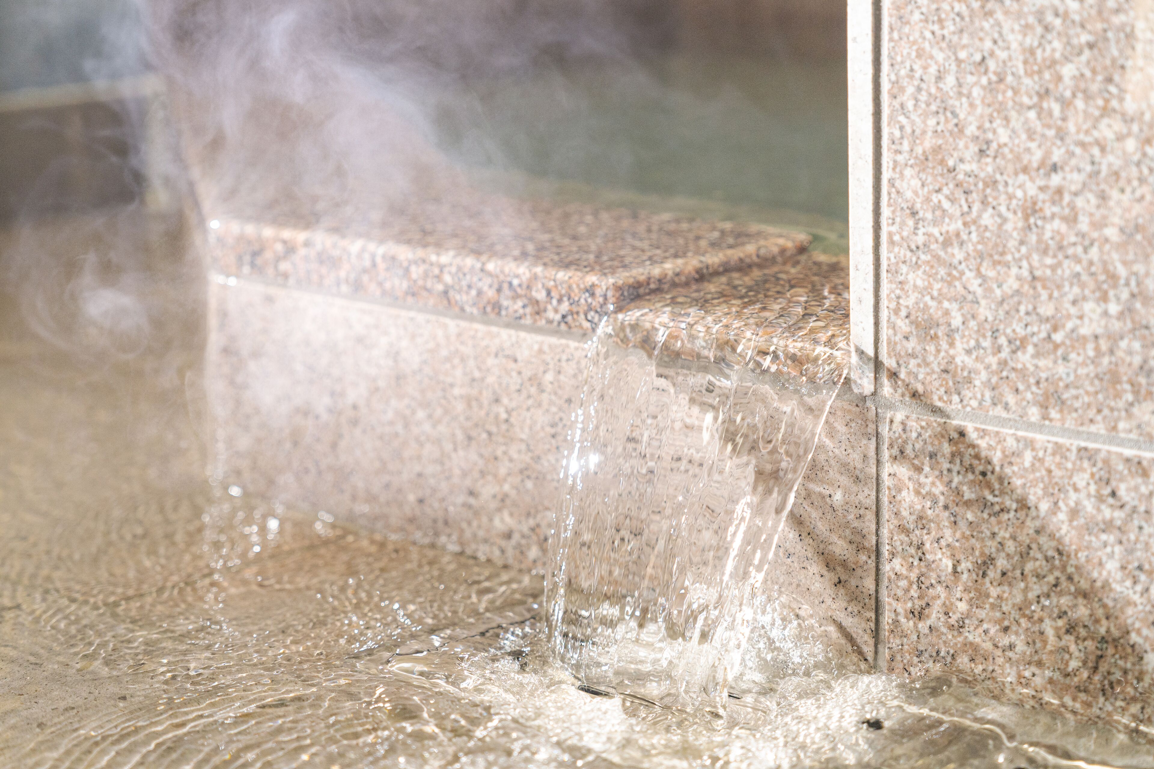 A close-up of a water feature with a clear, flowing stream over a textured stone surface.
