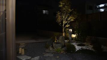 A nighttime view of a garden with a tree, rocks, and a building in the background.