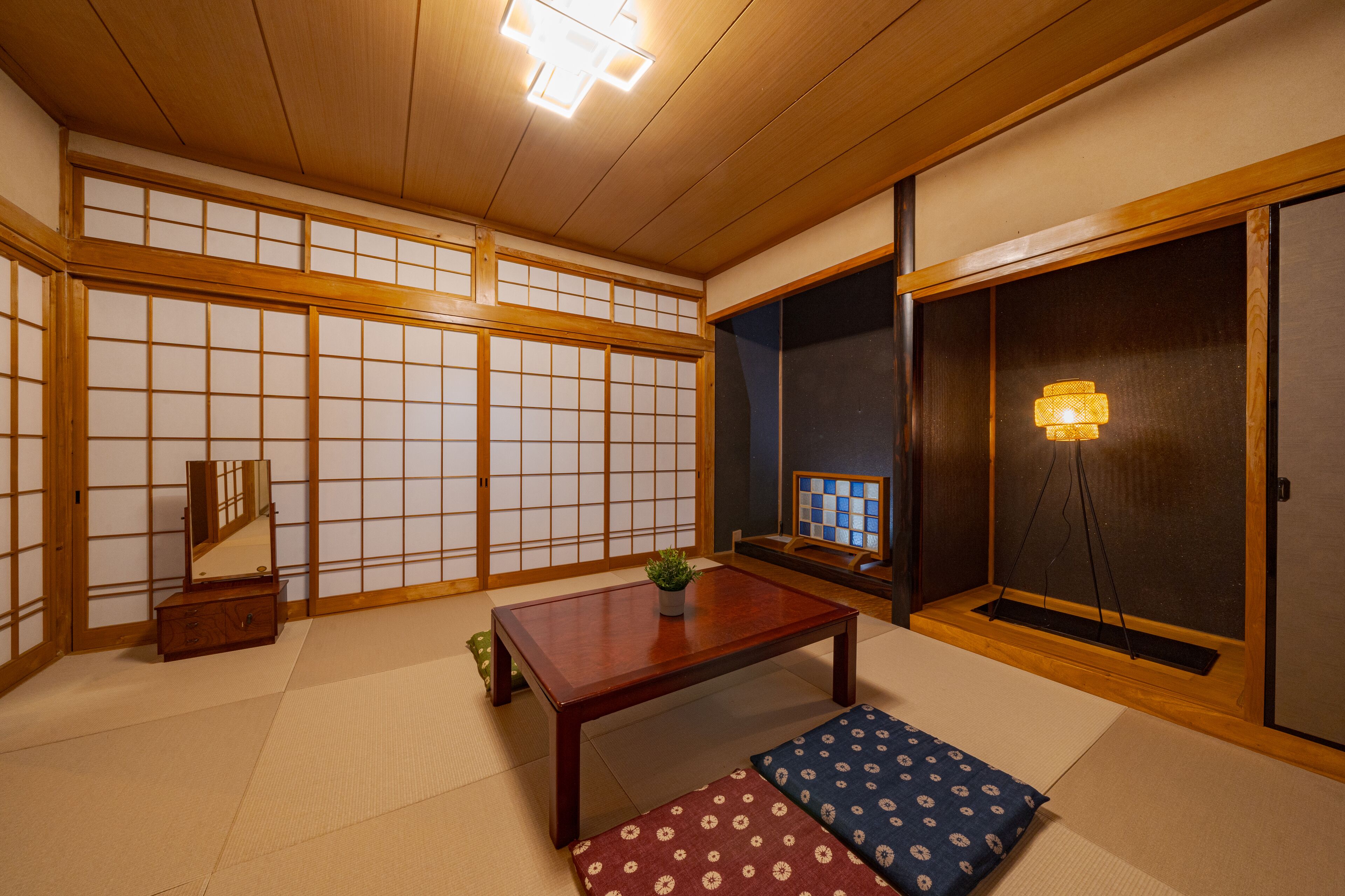 Una habitación japonesa tradicional con suelo de tatami, una mesa baja de madera, un mueble pequeño y puertas correderas.
