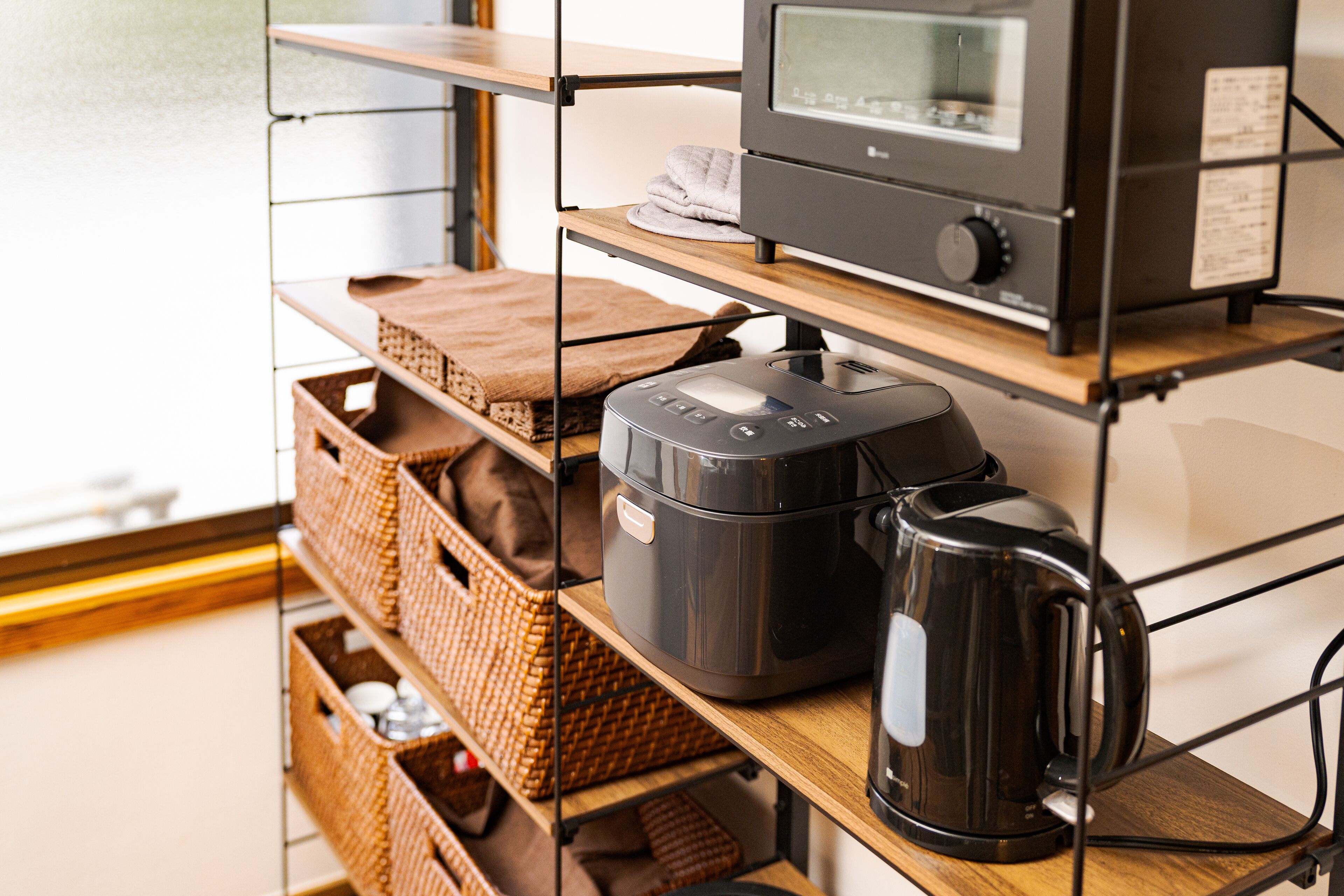 A kitchen area with a coffee maker, a rice cooker, and wicker baskets on shelves.