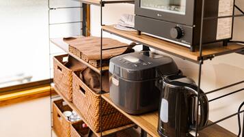 A kitchen area with a coffee maker, a rice cooker, and wicker baskets on shelves.