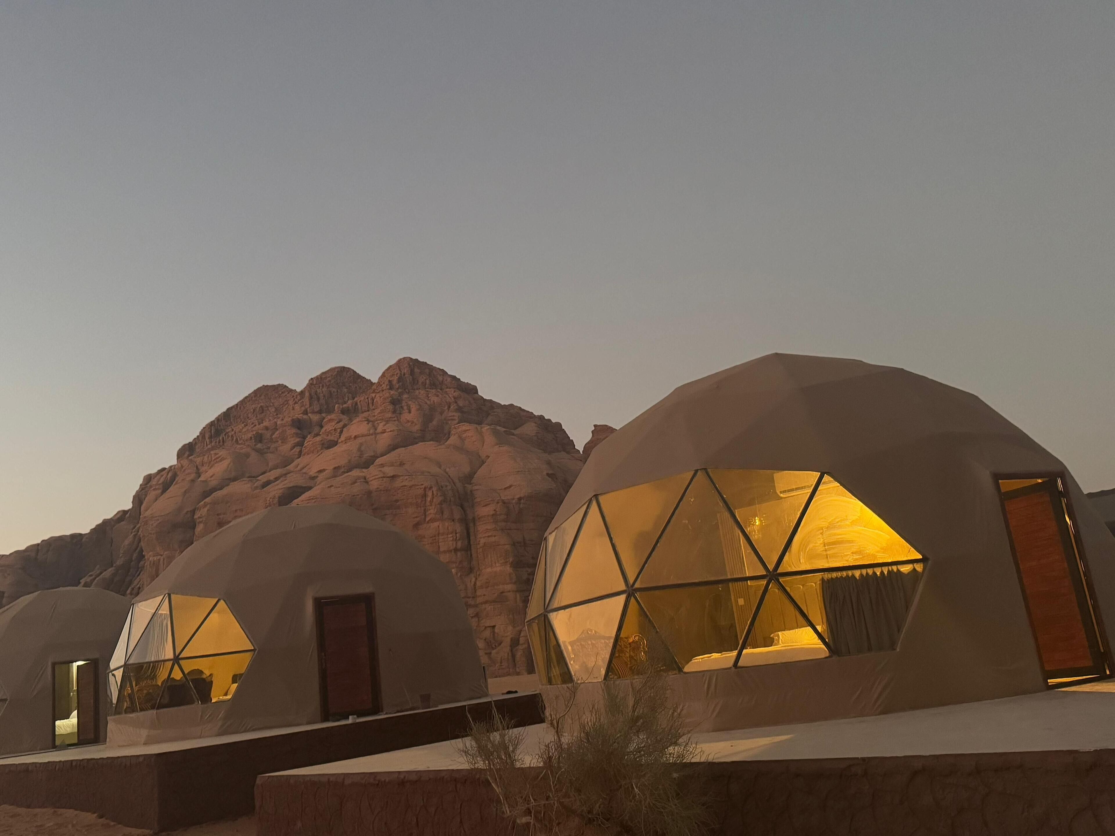 A row of dome-shaped accommodations with large windows, set against a mountainous backdrop.