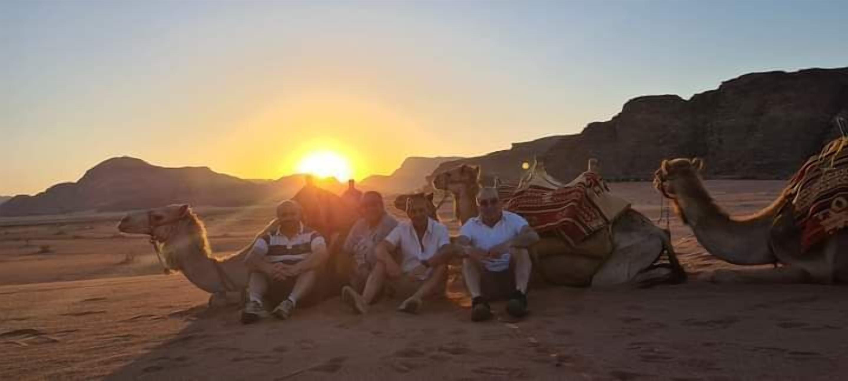 A group of people sitting on camels in a desert landscape at sunset.