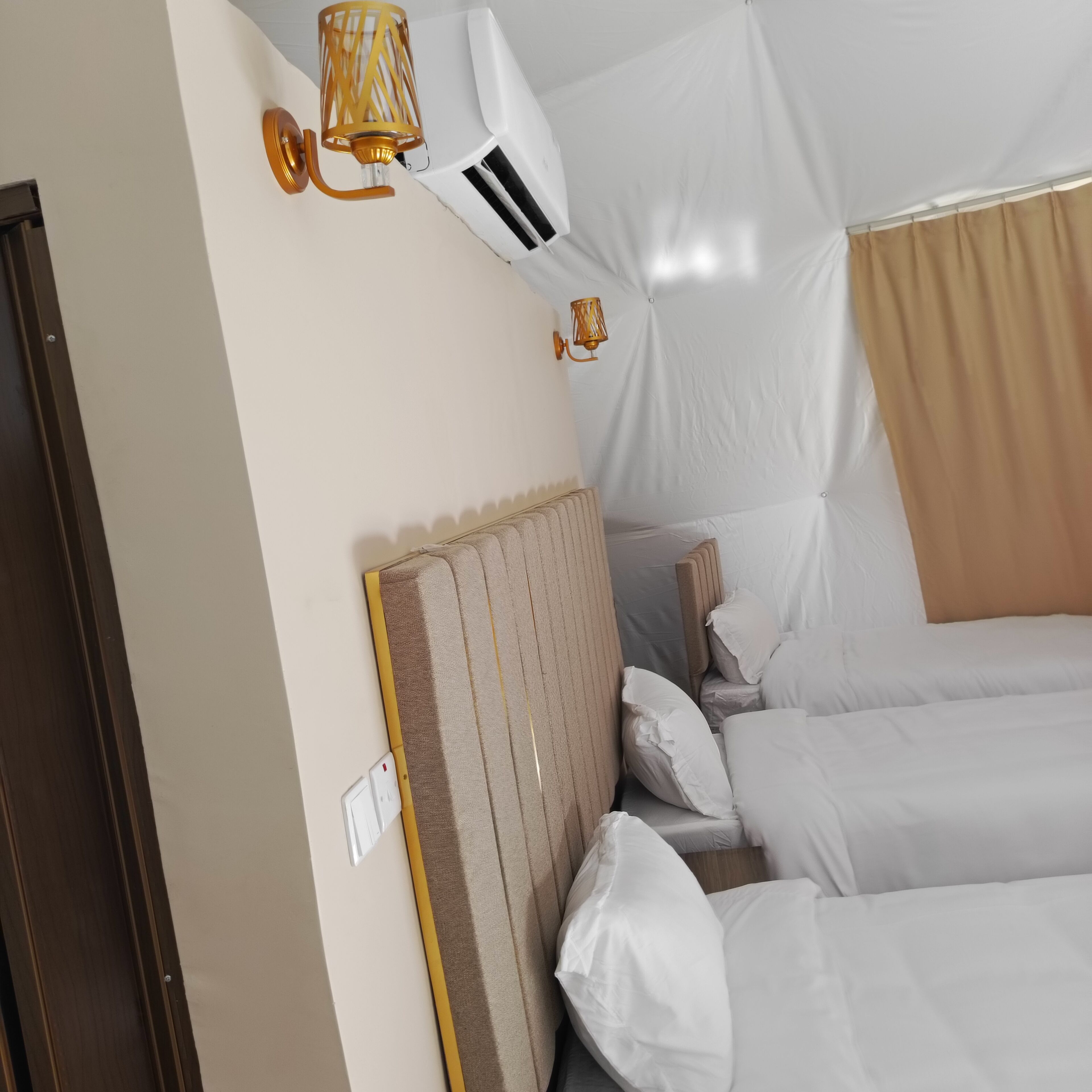 A hotel room with a large bed, a headboard, two wall-mounted lamps, and an air conditioning unit.