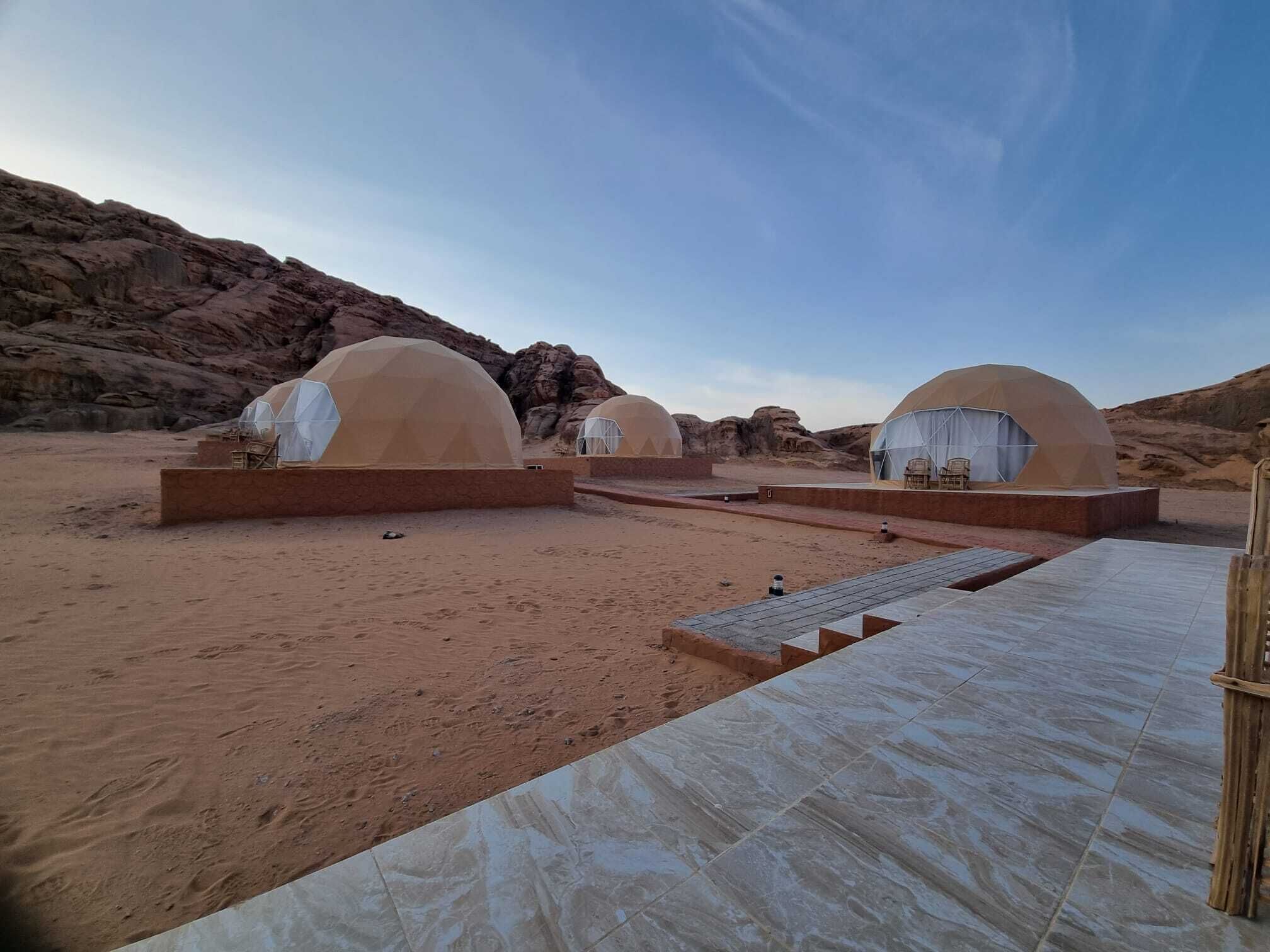 A desert landscape with three dome-shaped tents, each with a covered seating area and a small table.