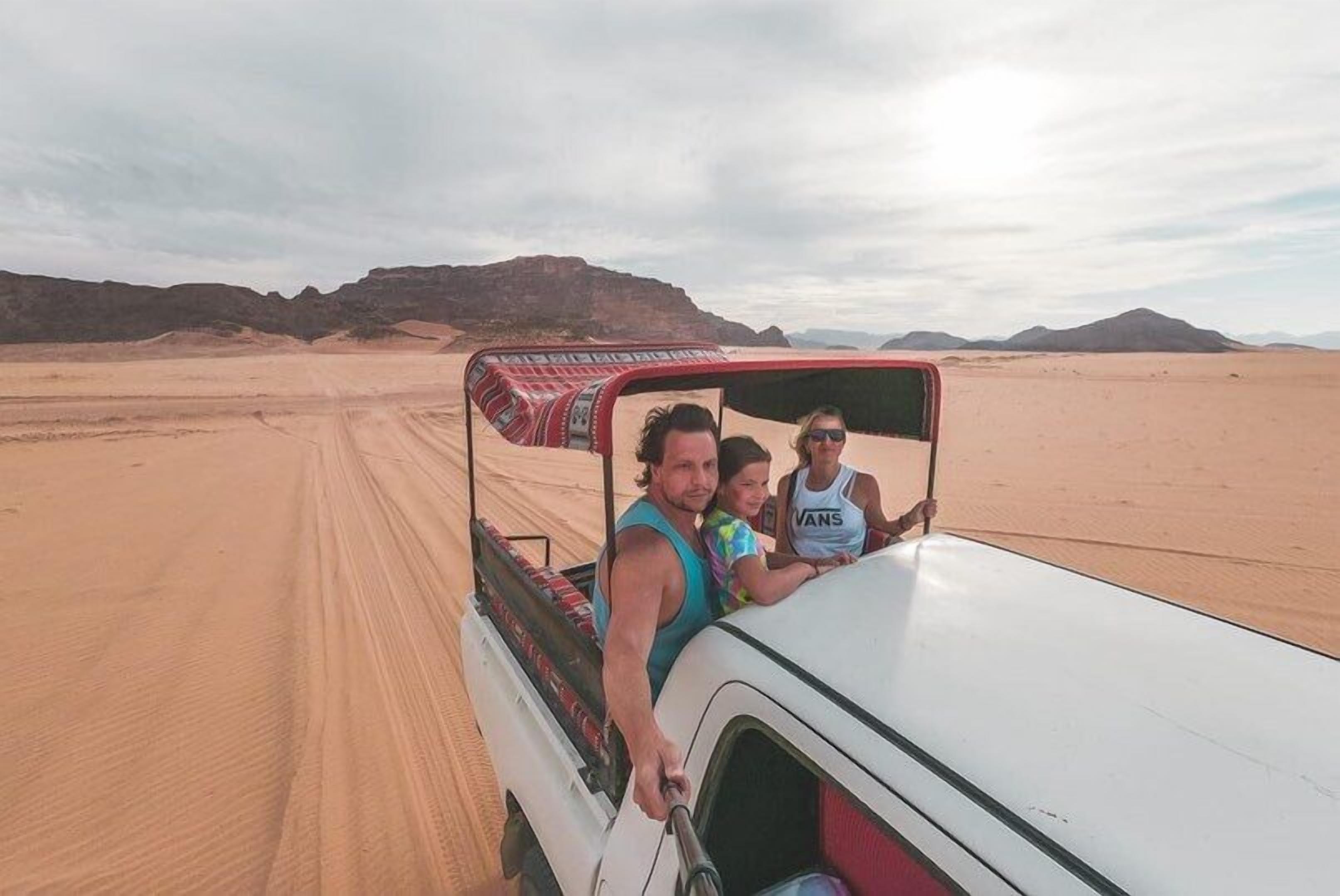 A desert landscape with a vehicle and three people.