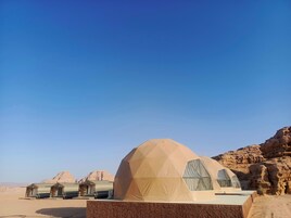 A desert landscape with a large geodesic dome tent and smaller structures.