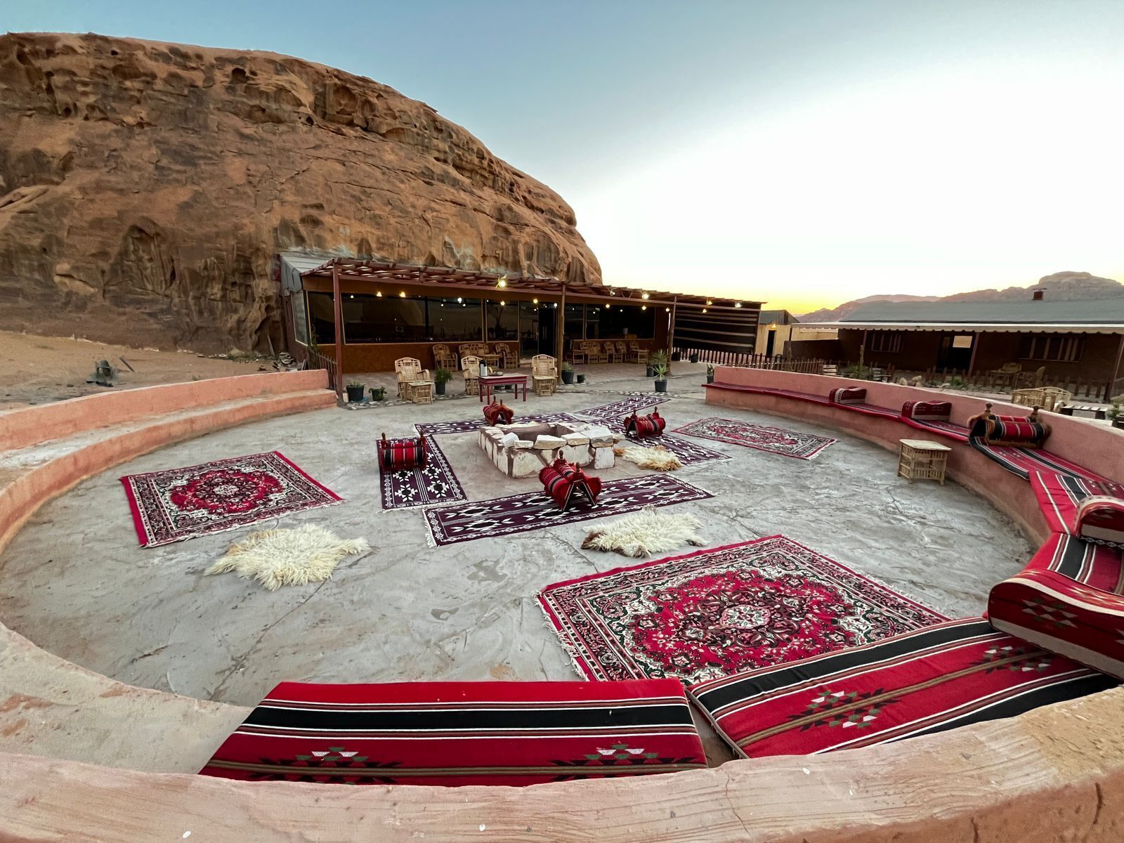 An outdoor seating area with rugs and furniture, a stage, and a mountainous backdrop.