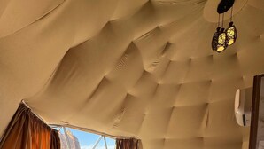 Quarto coberto por uma tenda, com uma cama, uma cadeira, uma mesinha e vista para a paisagem desértica.
