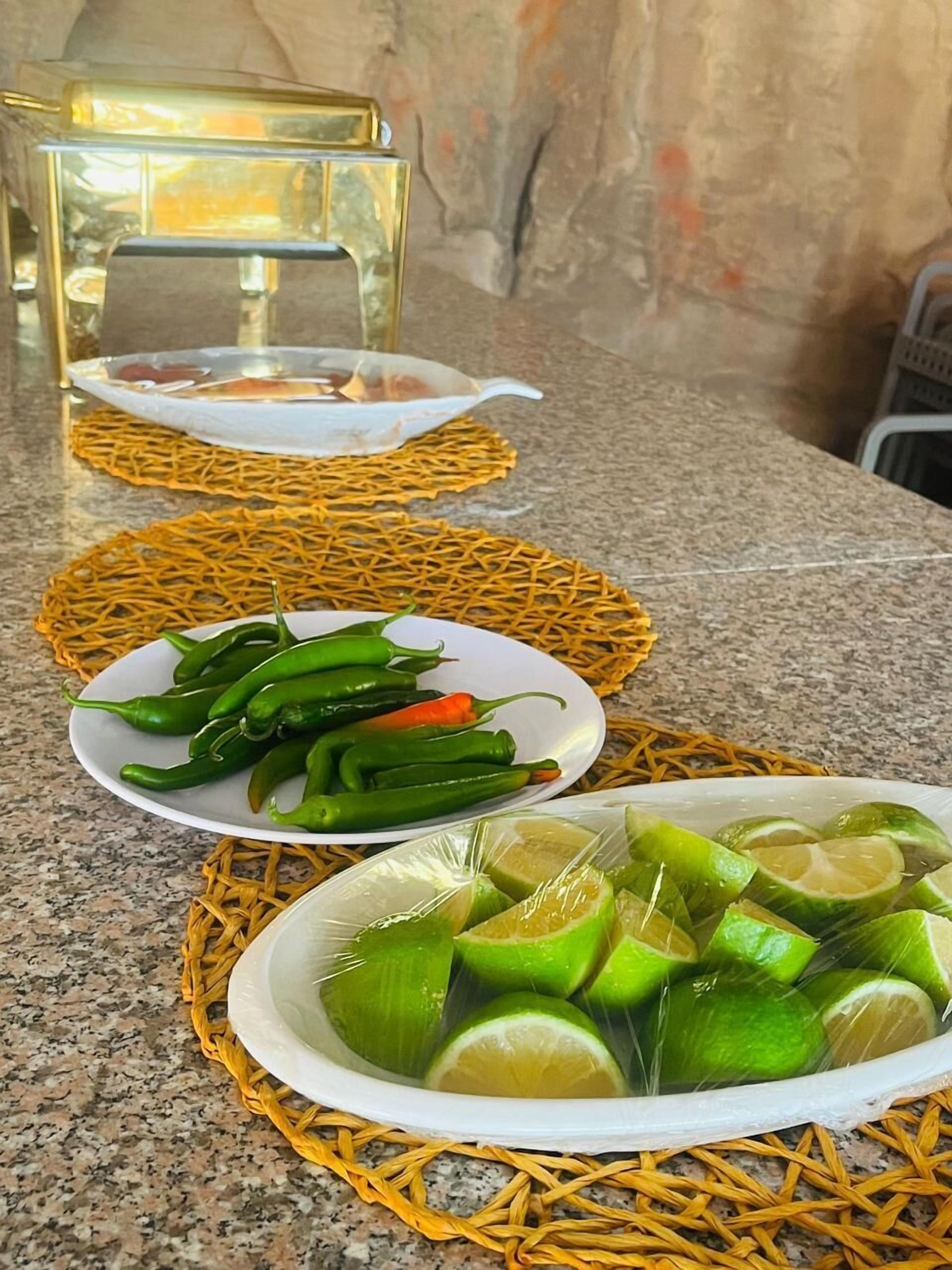 A kitchen counter with woven baskets containing green chili peppers and lime slices.
