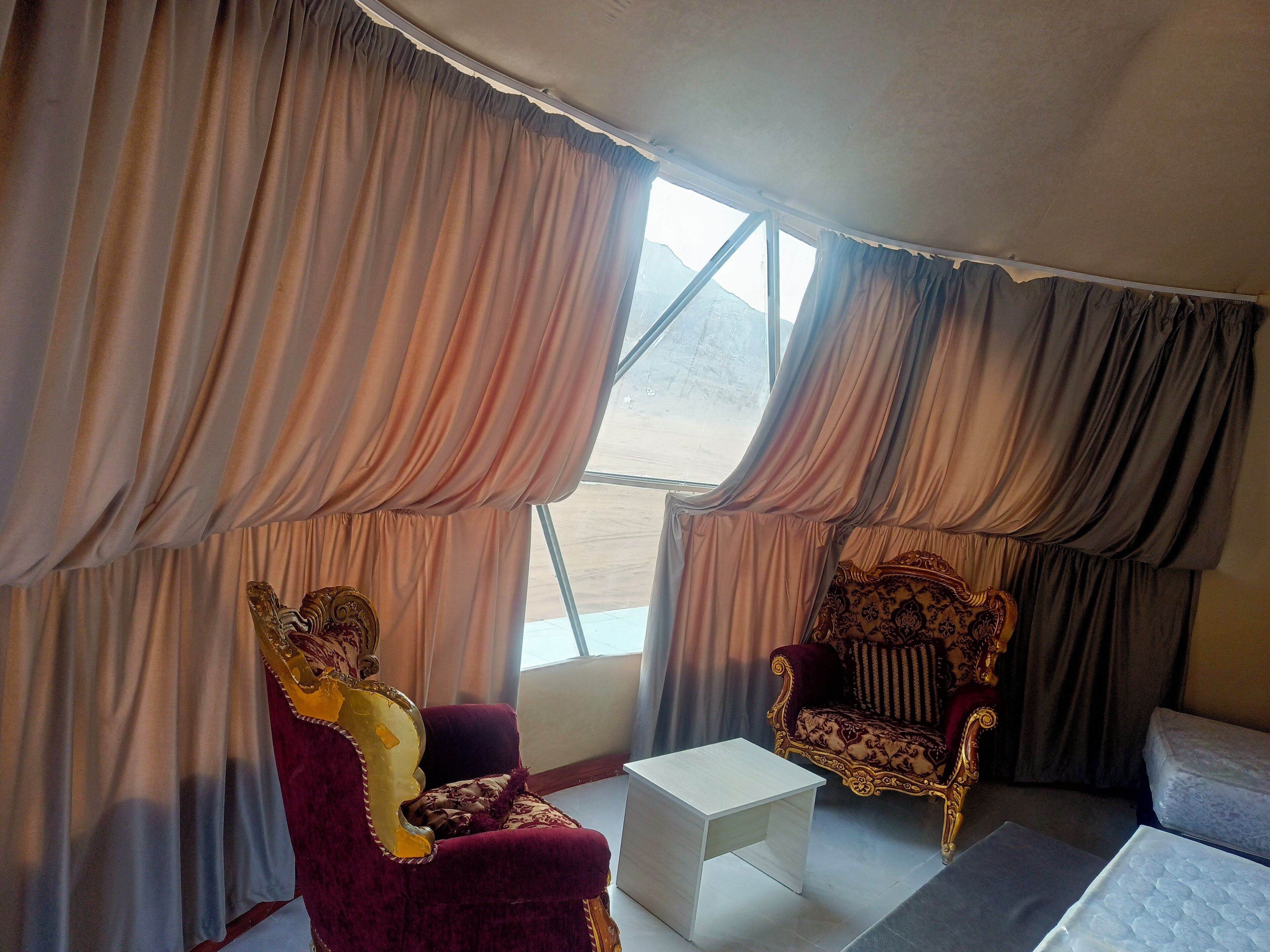 Una habitación con dos sillas decorativas, una pequeña mesa blanca y una cama.