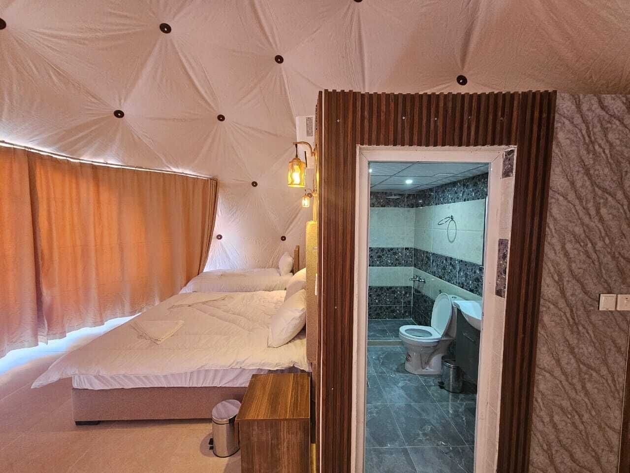 A compact room with a bed, a small wooden table, and a view into a bathroom with a toilet and sink.