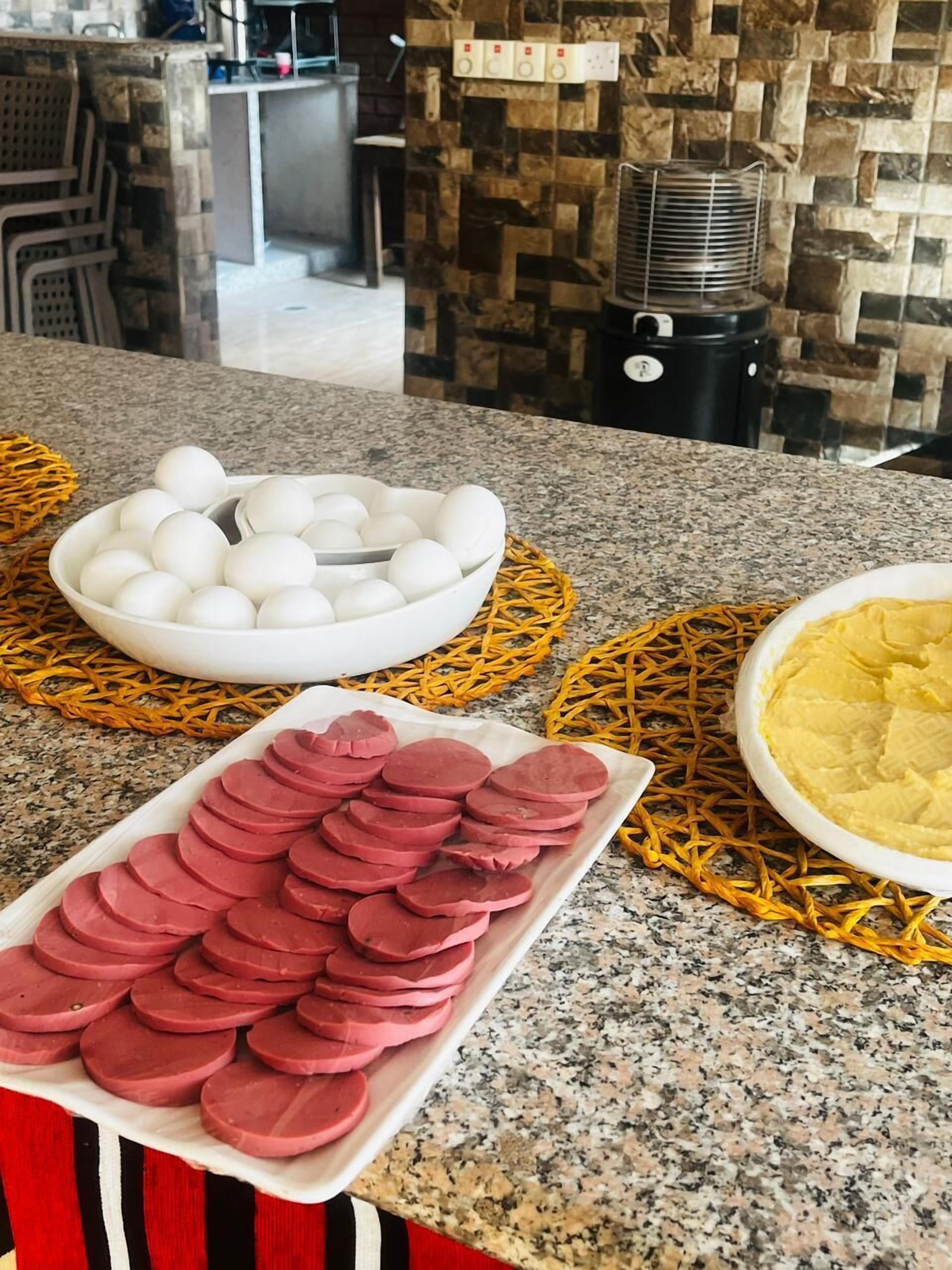 A kitchen counter with a bowl of eggs, a plate of sliced meat, and a bowl of mashed potatoes.