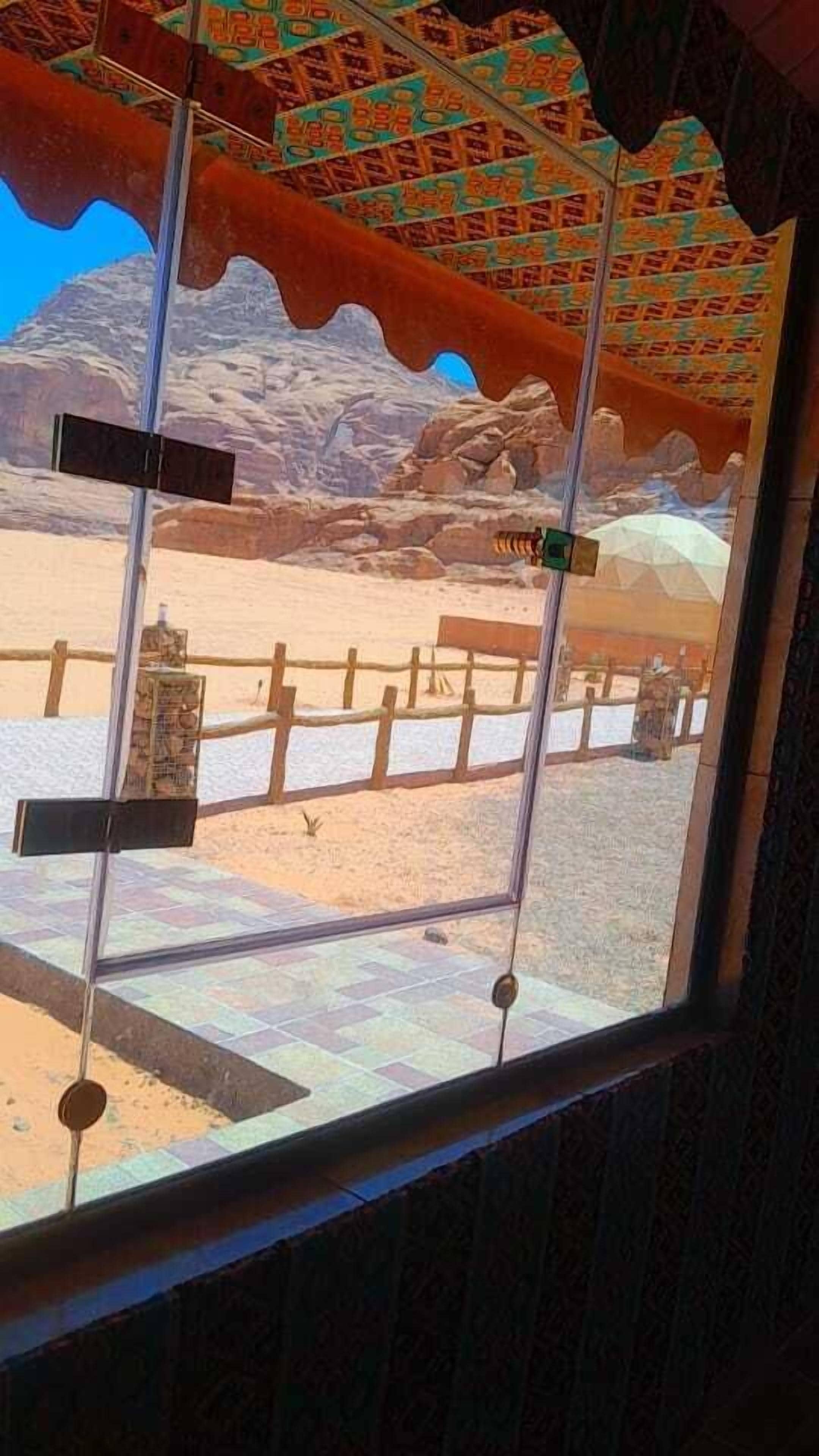 A window view of a desert landscape with a wooden fence and a rocky mountain in the background.
