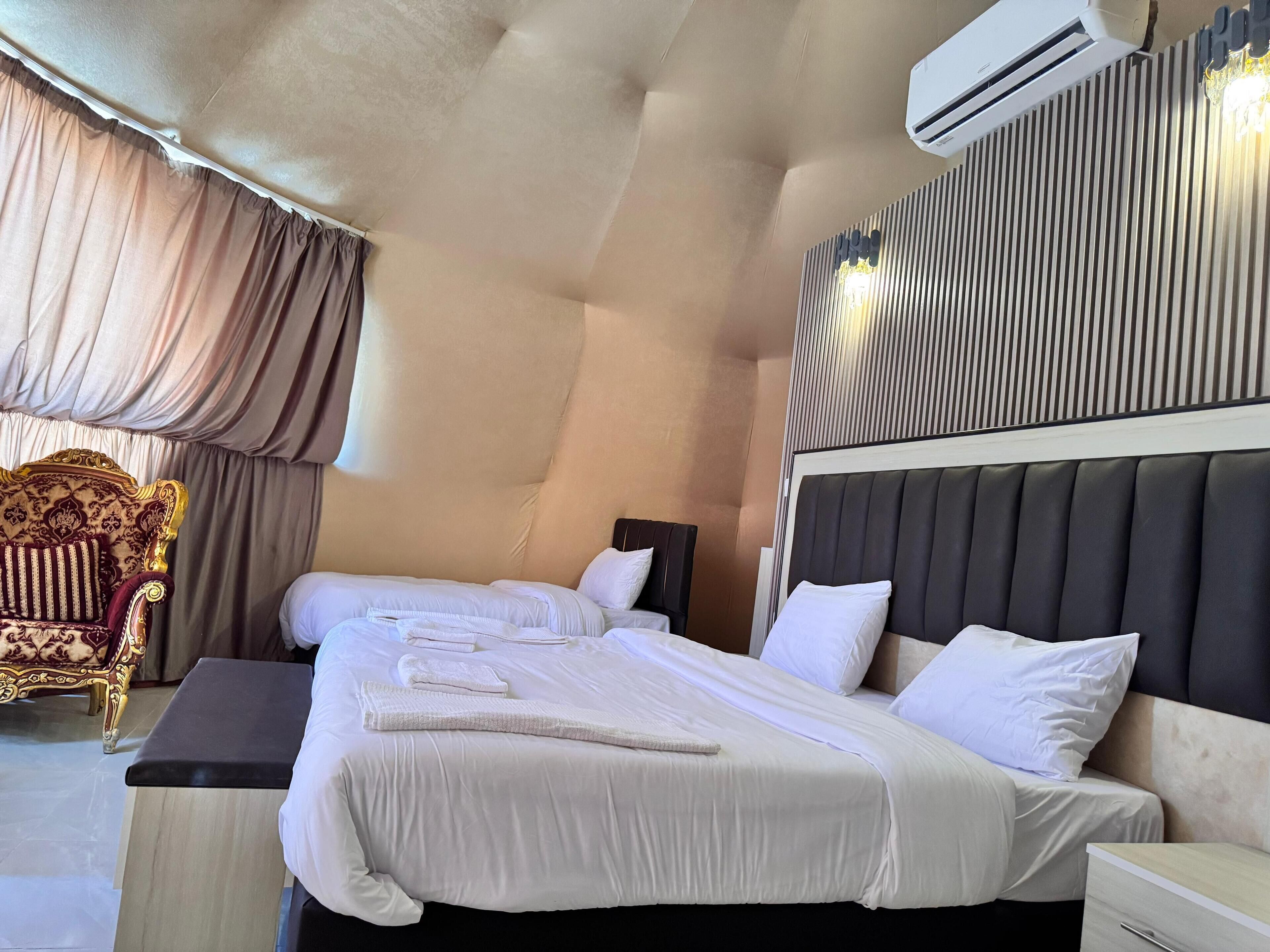 A hotel room with two beds, a large window with curtains, a decorative chair, and an air conditioning unit.
