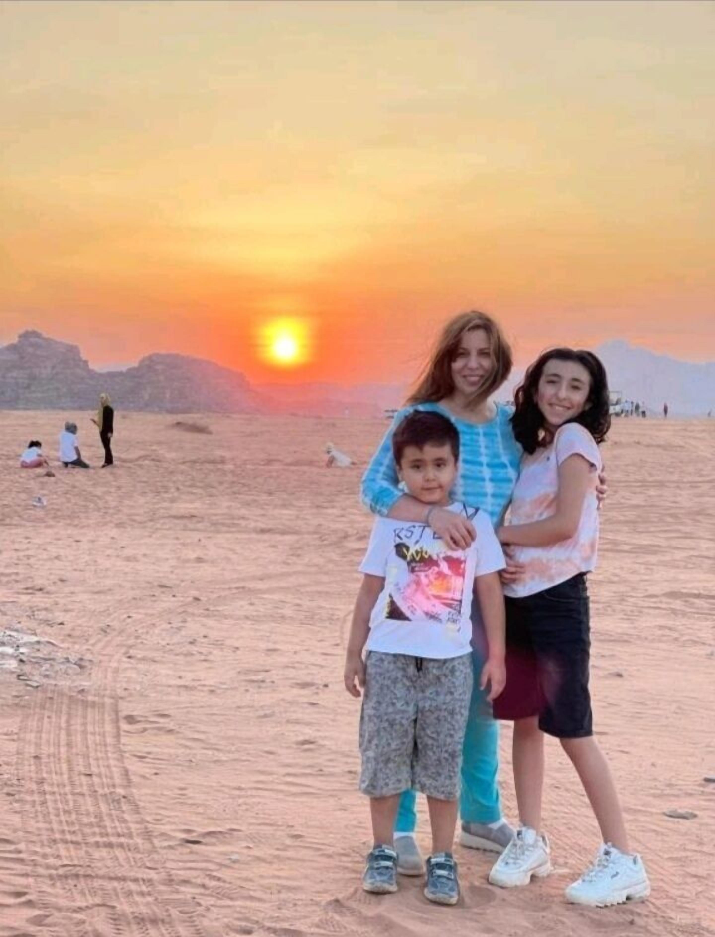 A family standing on a sandy beach with a sunset in the background.