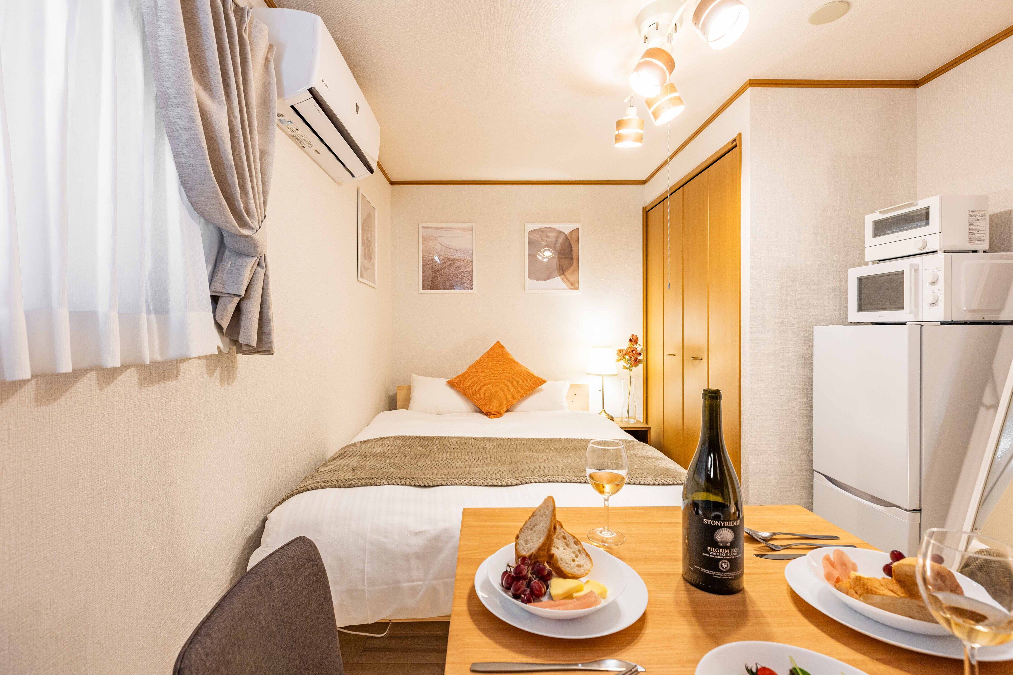 Une chambre d’hôtel avec un lit, une table à manger avec des assiettes de nourriture et une bouteille de vin, un four à micro-ondes et un réfrigérateur.