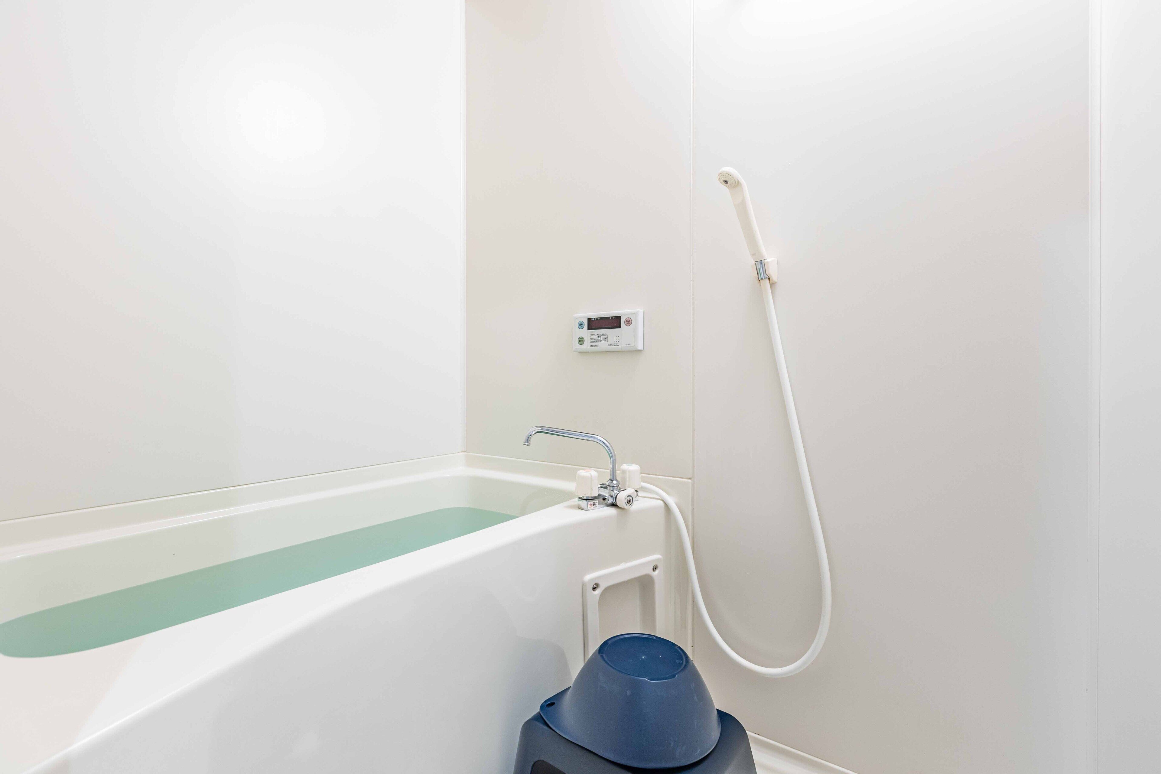 Een badkamer met een bad, een handdouche en digitale temperatuurregeling.