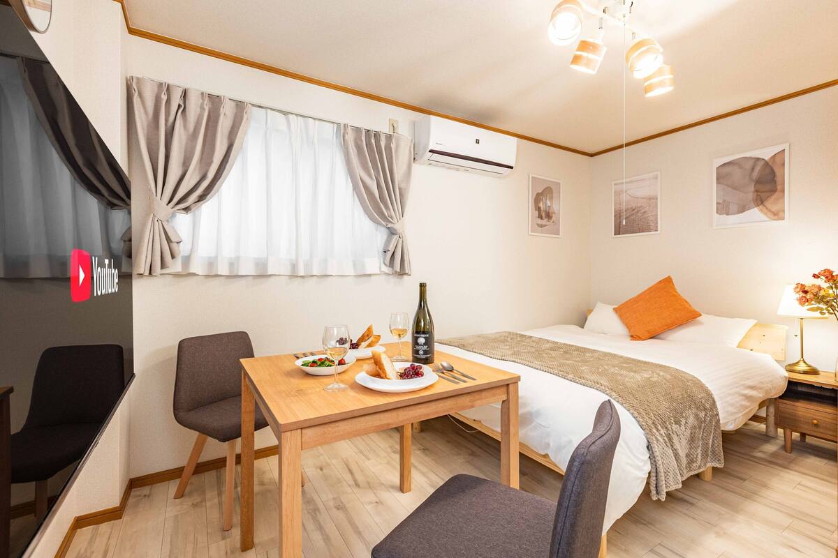 Ein Hotelzimmer mit einem Bett, einem Esstisch mit Stühlen, einem Fernseher und einem Fenster mit Vorhängen.