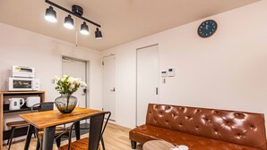 A modern kitchen with a wooden table, chairs, a brown leather sofa, and a clock on the wall. - Arita biru daikoku (Osaka)