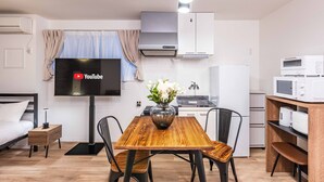A modern kitchen with a flat-screen TV, wooden dining table, and white cabinets. - Arita biru daikoku (Osaka)