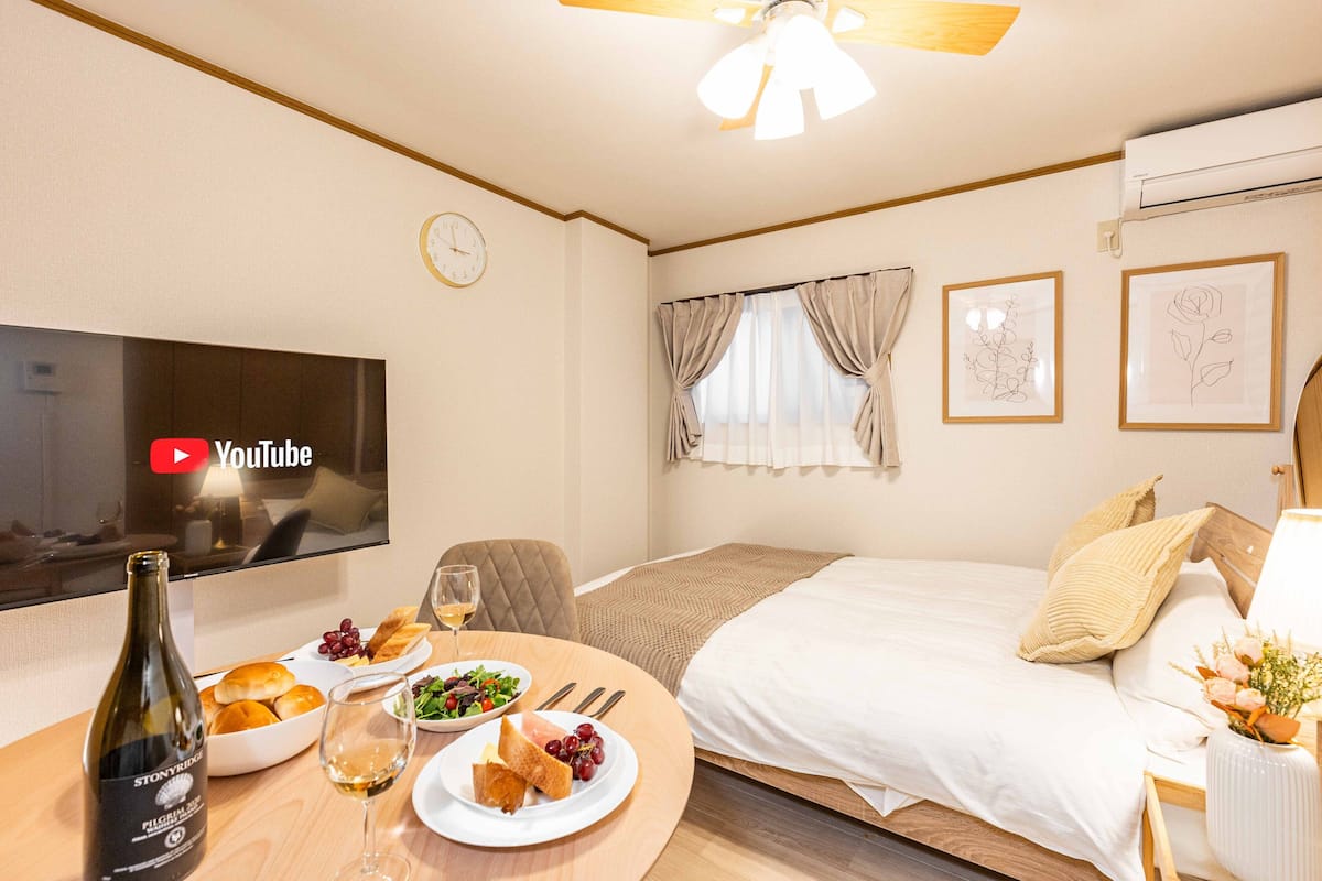 Ein Hotelzimmer mit Bett, Fernseher, Esstisch mit Speisen und Getränken sowie einem Fenster mit Vorhängen.