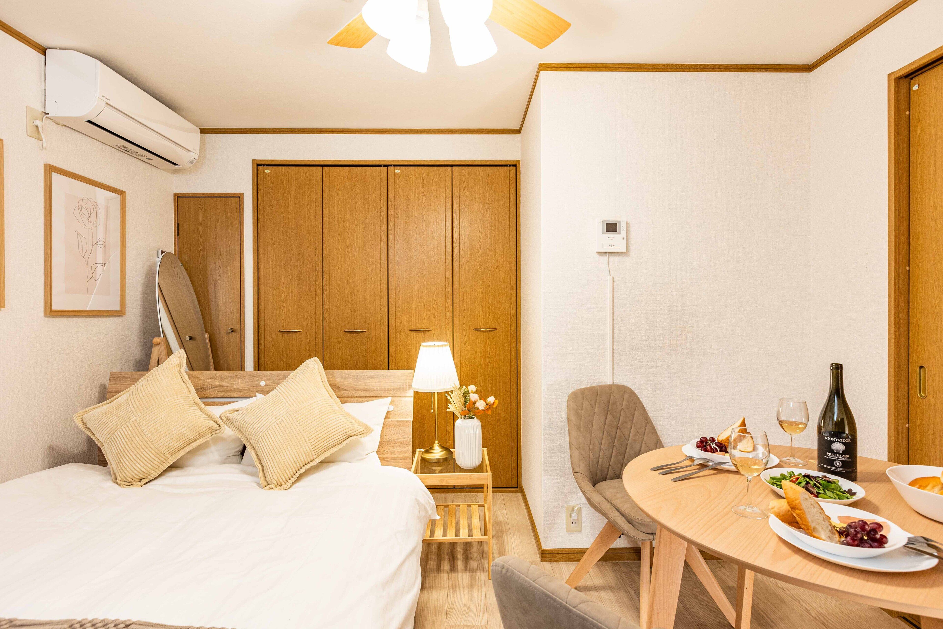 Une chambre d’hôtel avec un lit, une table de chevet, une lampe, une chaise, une table à manger avec des assiettes, du vin et une bouteille.