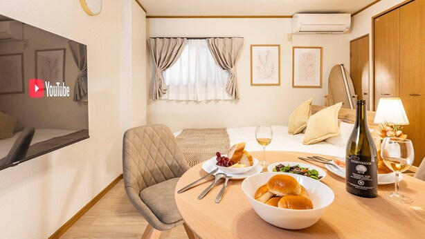 A hotel room with a bed, a dining table with food and wine, a chair, a TV, and a ceiling fan. - Arita biru daikoku (Osaka)