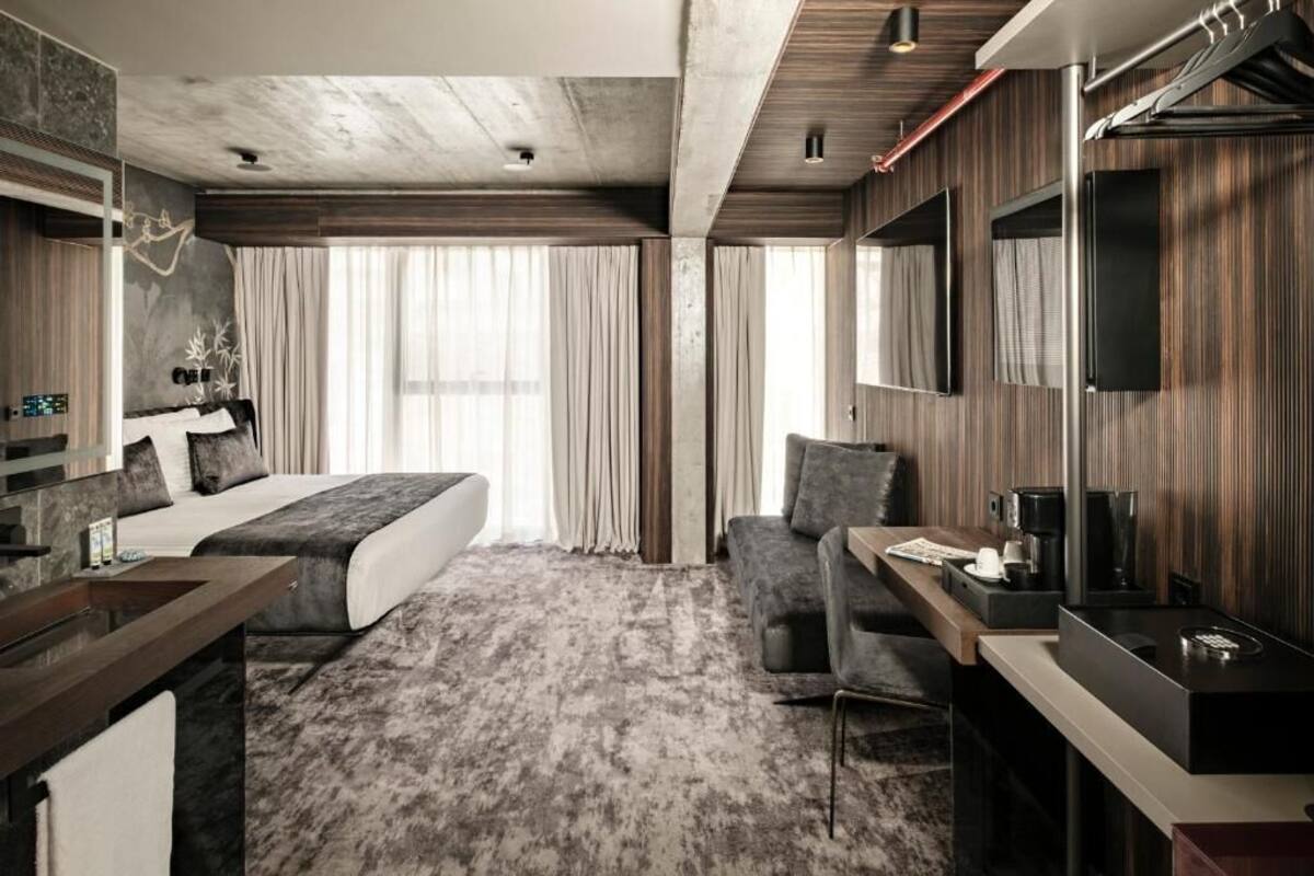 Una habitación de hotel moderna con cama, escritorio, silla, televisión y un ventanal grande.