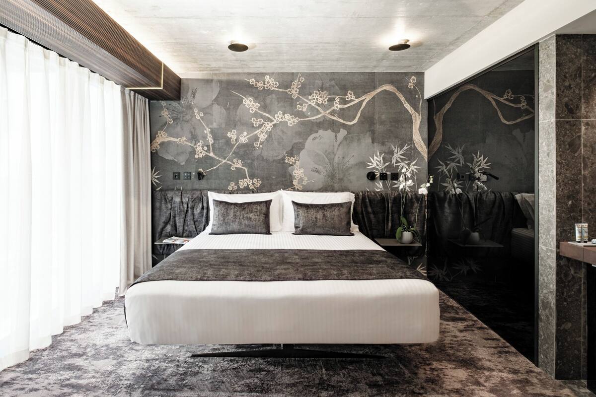 Un dormitorio moderno con una cama grande, arte mural oscuro y vistas a la ciudad.