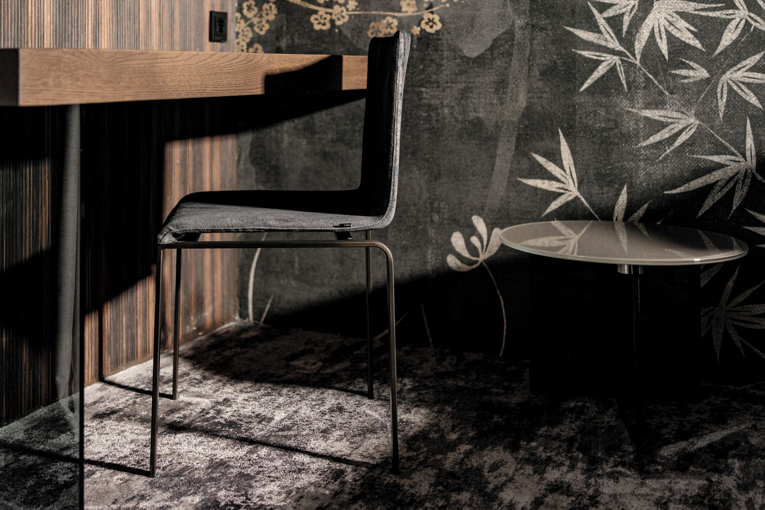 A modern room with a minimalist design, featuring a black upholstered chair, a small round table, and a patterned wall.