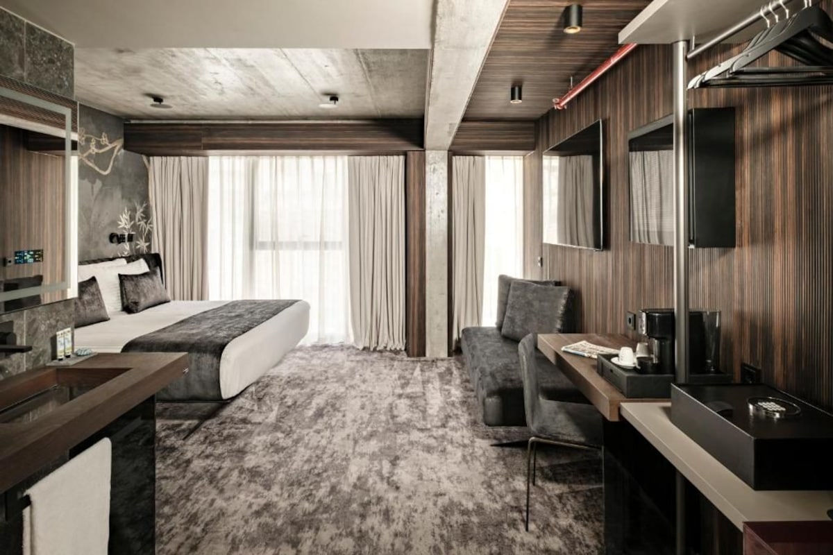A modern hotel room with a bed, a desk, a chair, a TV, and a large window.