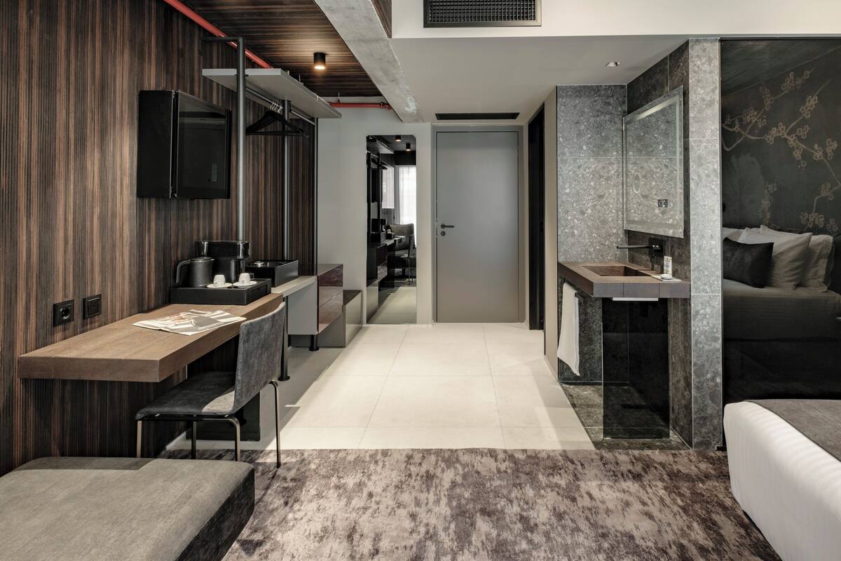 Una habitación de hotel moderna con una pared decorativa de madera, un televisor de pantalla plana, una kitchenette y un baño de mármol, además de un sofá cama.
