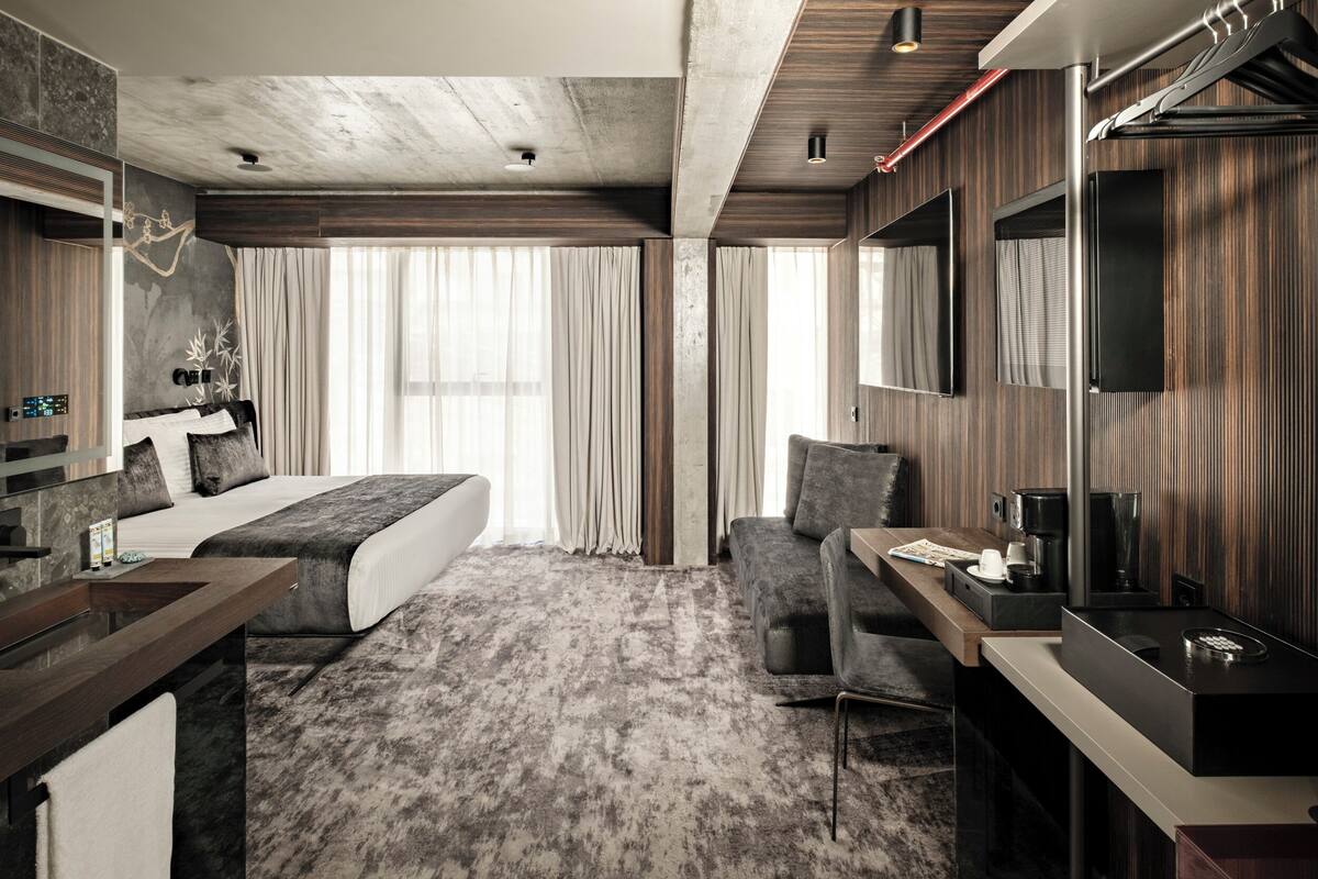 Una habitación de hotel moderna con una cama grande, un escritorio, una silla, un televisor y un espacio para el baño.