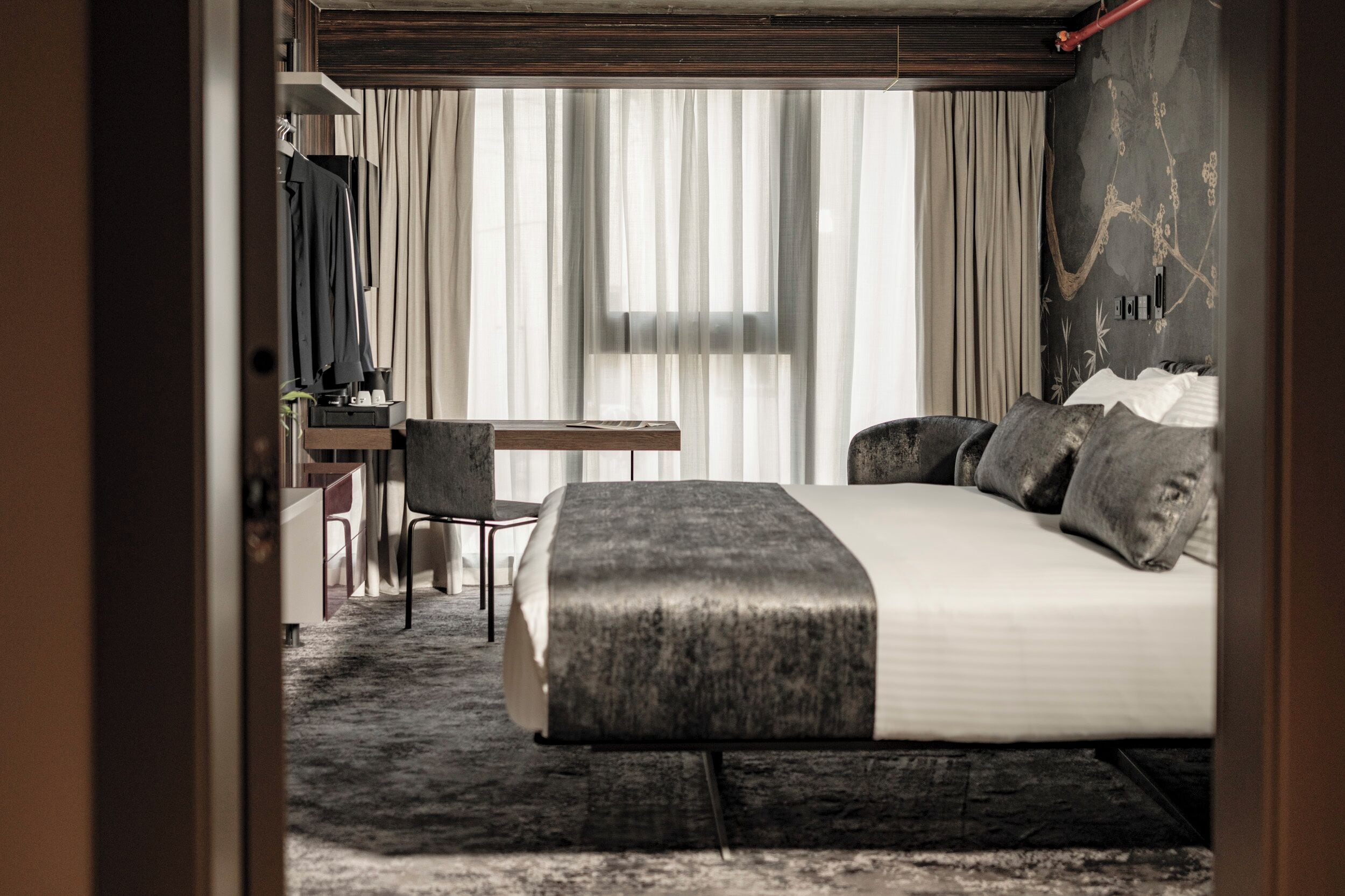 A modern hotel room with a large bed, a desk, and a chair.