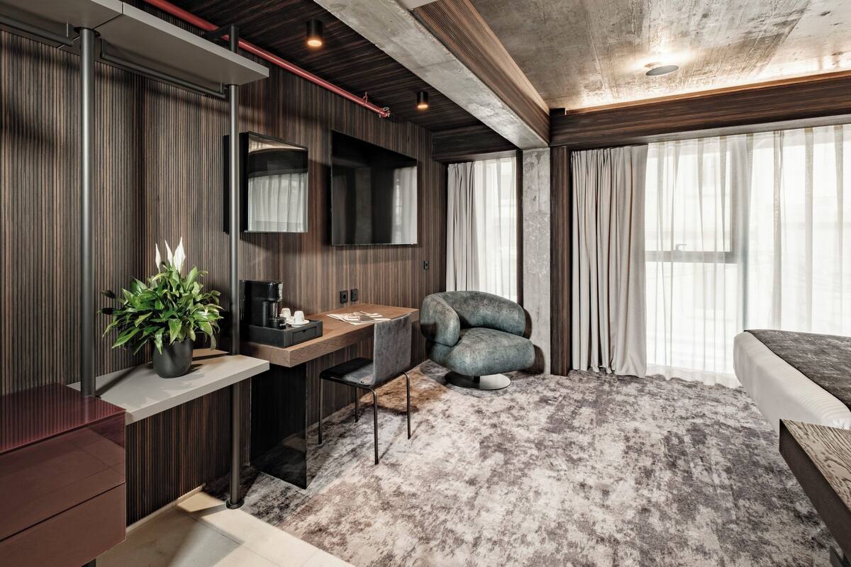 Un dormitorio moderno con una cama grande, un escritorio con silla, una planta en maceta y un ventanal con cortinas.