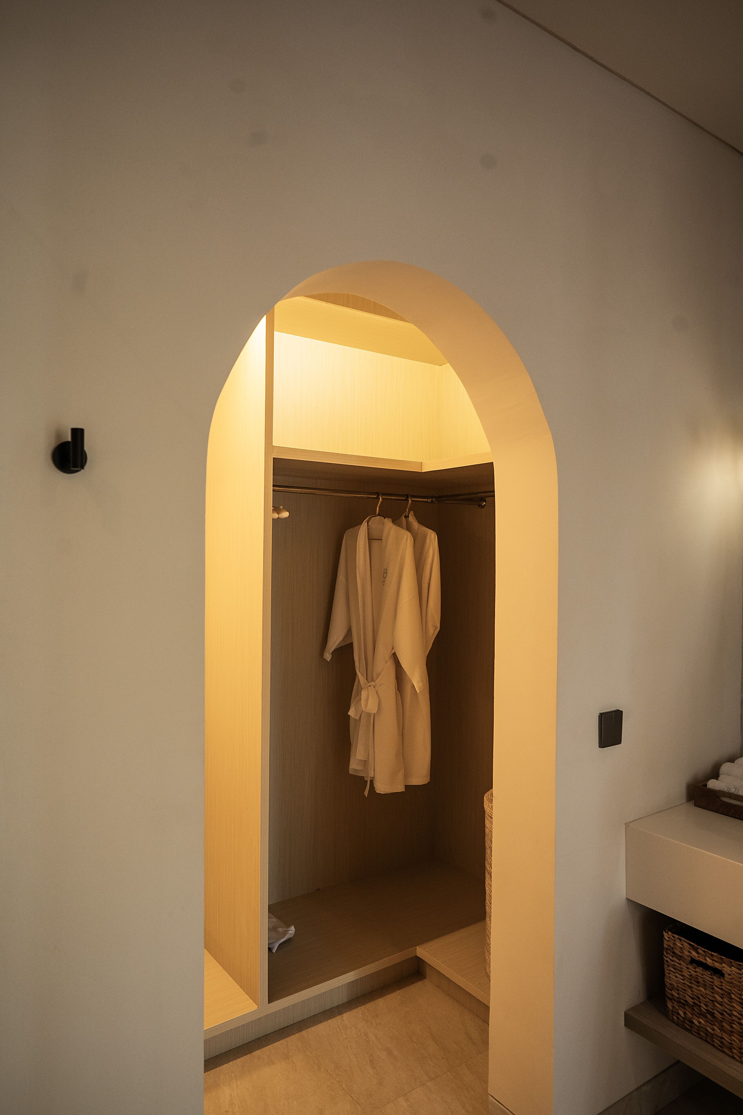A walk-in closet with a robe hanging on a rack, a wooden floor, and a white wall with a small shelf.