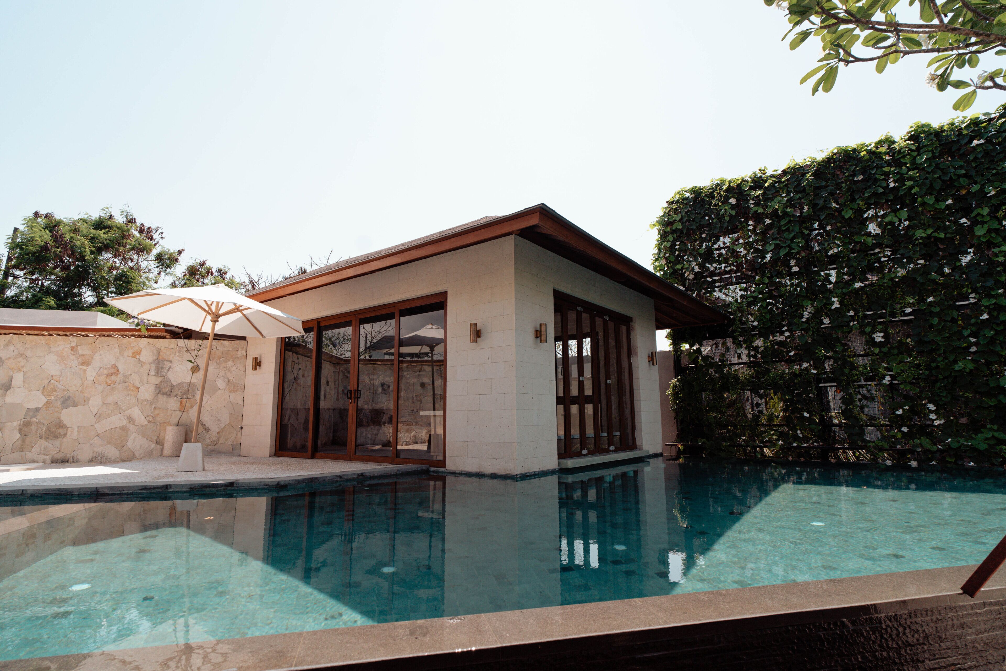 A modern house with a swimming pool, stone wall, and large glass doors.