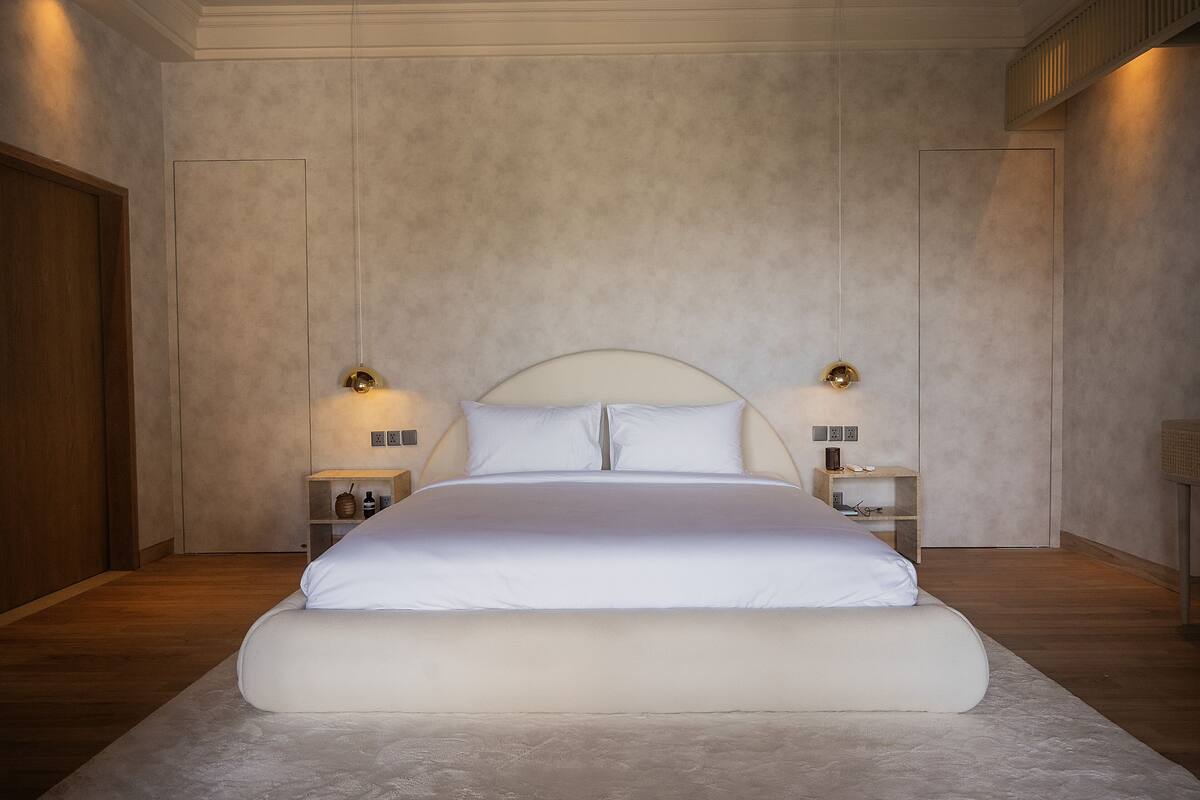 A modern bedroom with a large bed, two bedside tables with lamps, and a wooden floor.