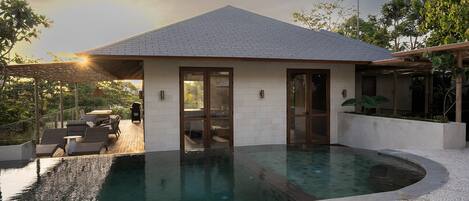 Ett modernt hus med en swimmingpool, stora glasdörrar och en täckt uteplats.