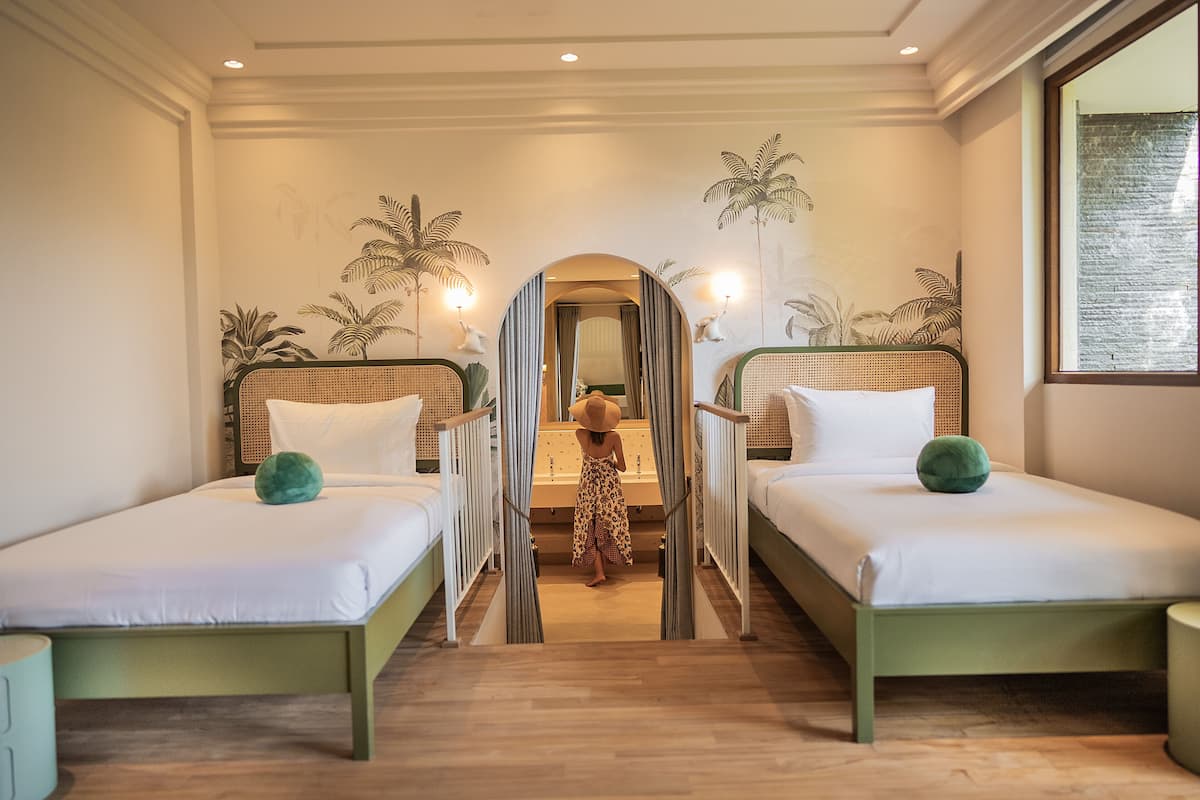 A hotel room with two single beds, a mirror, and a view of the hallway.