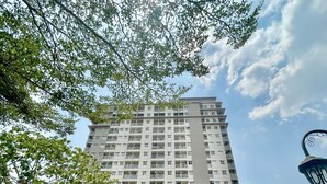 A high-rise building with a central entrance, surrounded by greenery and a clear sky.