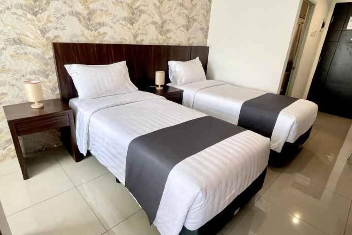 A hotel room with two beds, a nightstand, and a lamp.