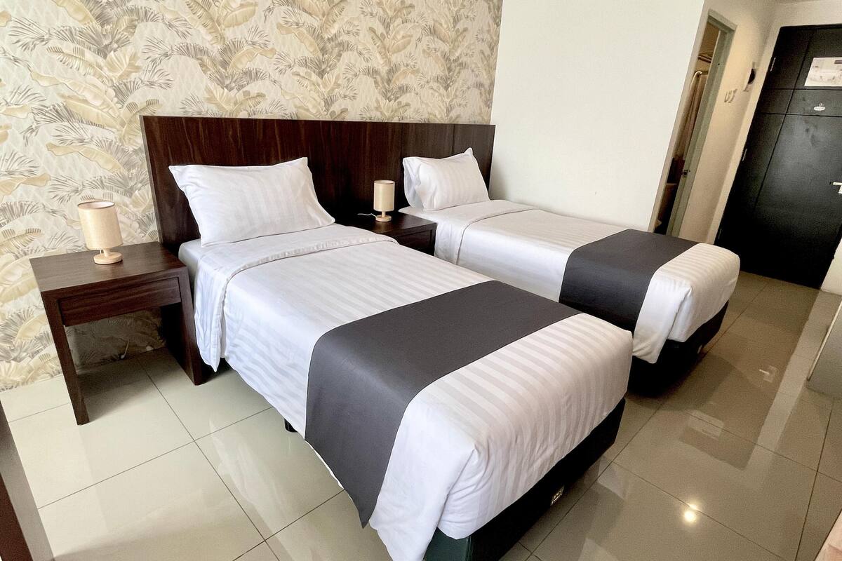 A hotel room with two beds, a nightstand, and a lamp.