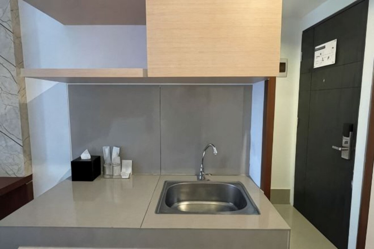 Una cocina moderna con un lavamanos de acero inoxidable, un cubo de basura negro y un armario de madera sobre el lavamanos.