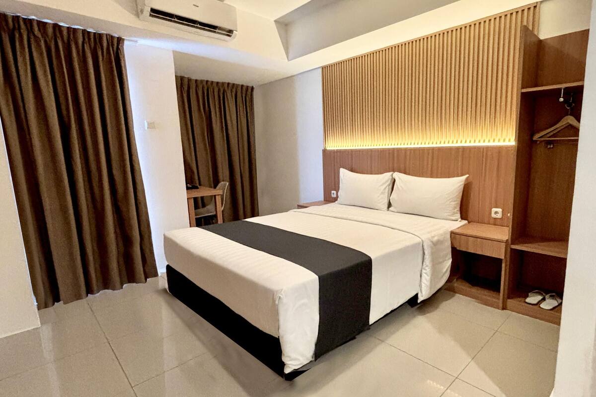 A hotel room with a bed, a wooden headboard, a bedside table, and a wardrobe.