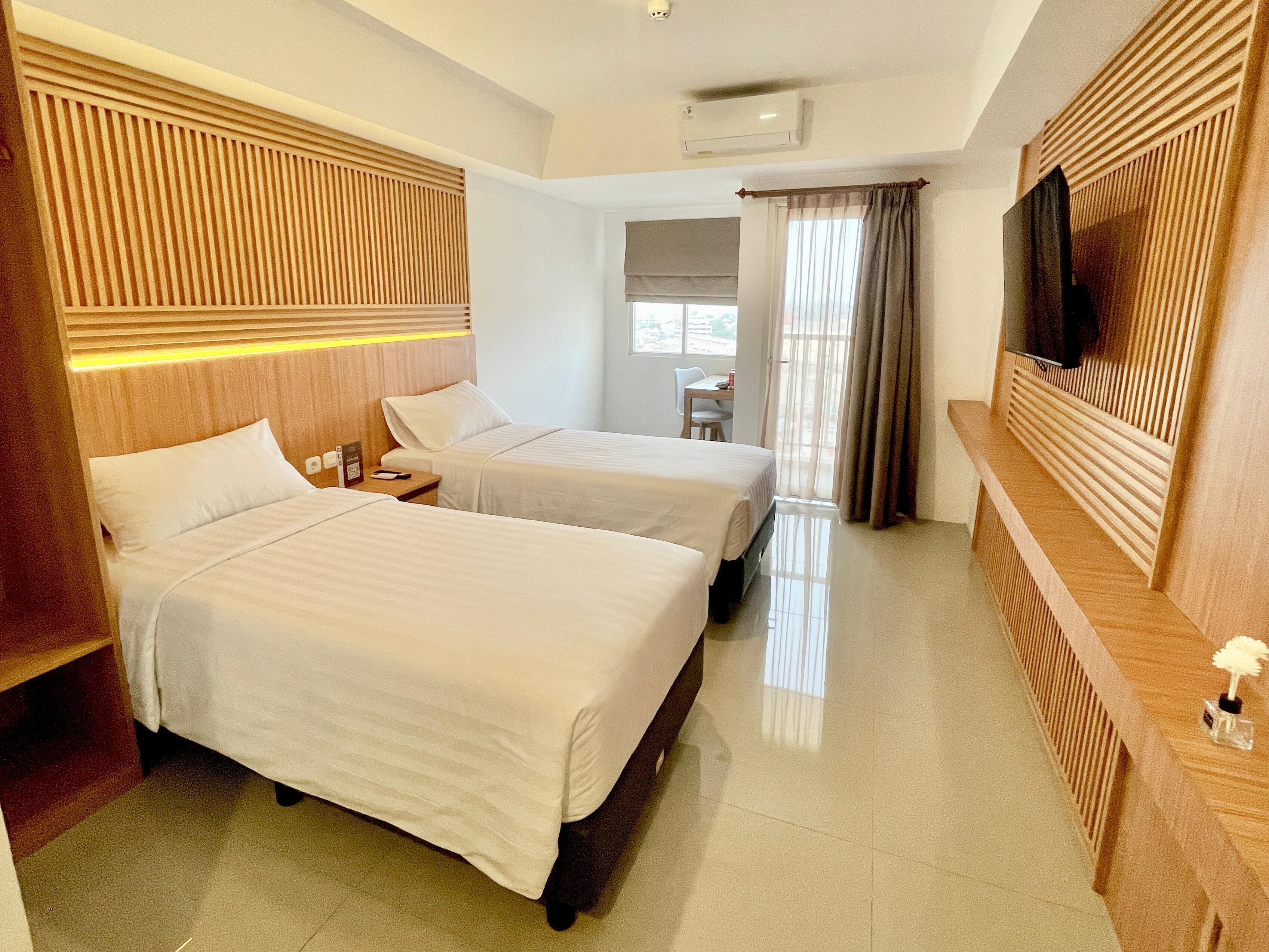 A hotel room with two beds, a TV, a desk, and a chair.