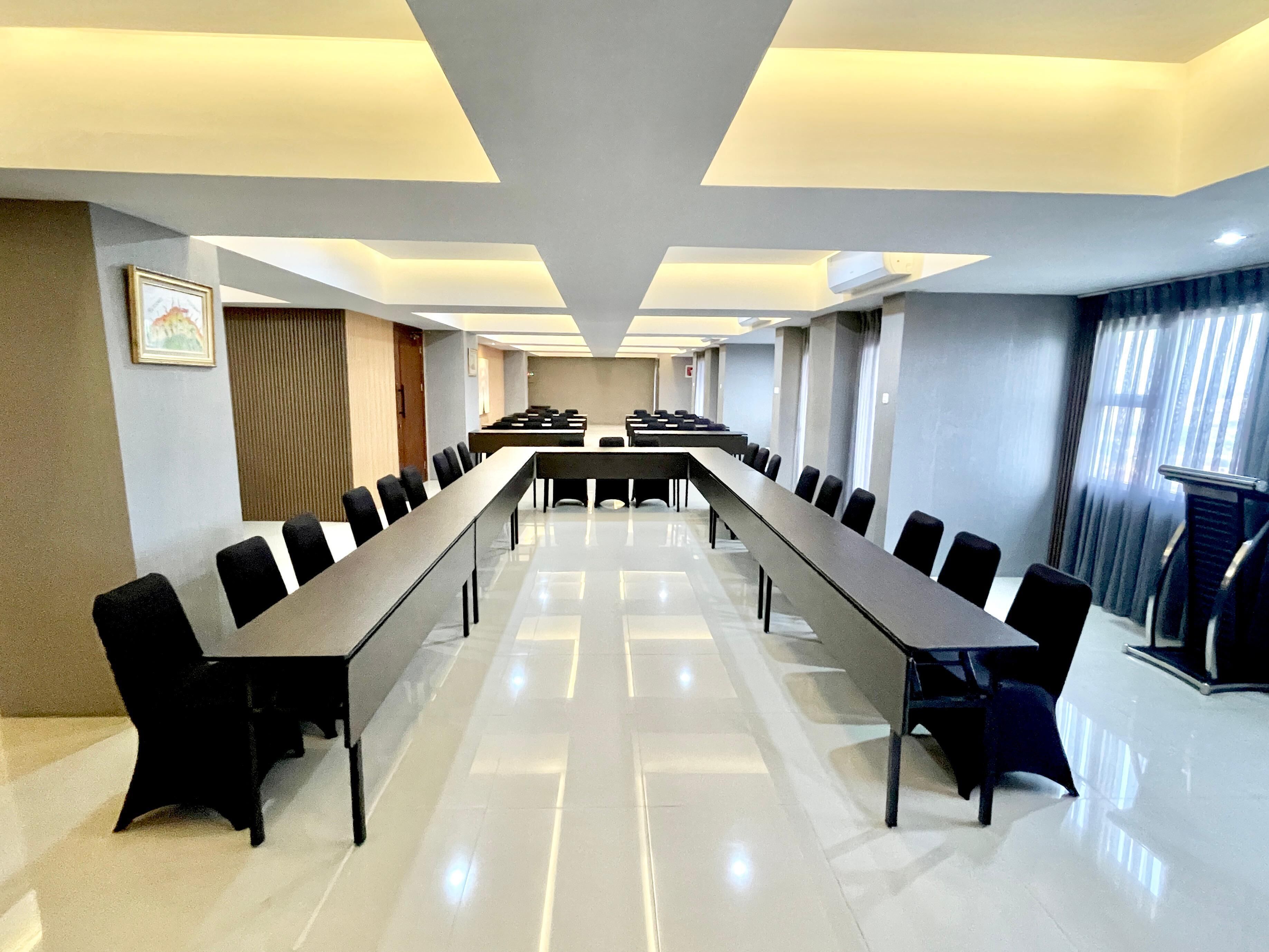 Un salón de conferencias con una larga mesa y sillas, un cuadro en la pared y una ventana con cortinas.
